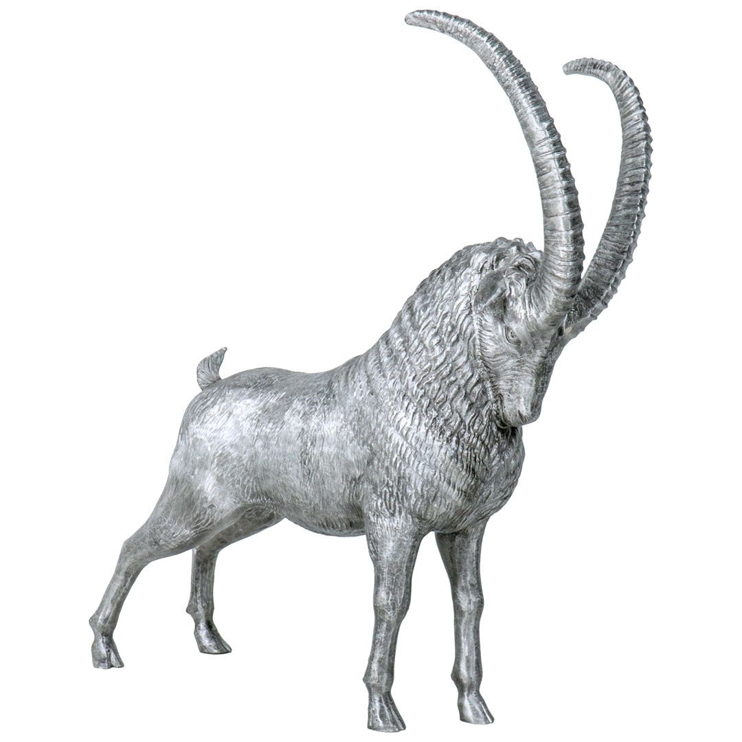 A metallic silver sculpture of an ibex or wild goat with long curved horns, shown in profile against a plain white background.