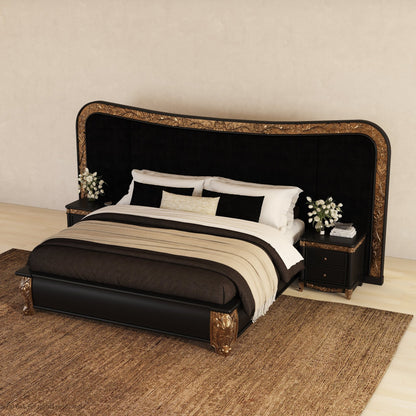 A luxury bed with a large black velvet headboard featuring ornate gold detailing, dressed in black, white, and beige bedding, flanked by two matching nightstands on a woven rug.
