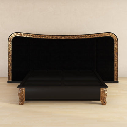 A black wooden bed frame with ornate gold carved details on the headboard, footboard, and legs, shown on a light wood floor against a beige wall.